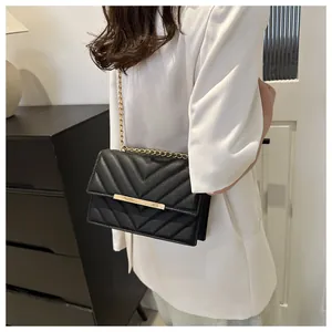 Dettaglio borsa trapuntata nera con catena dorata indossata su blazer bianco