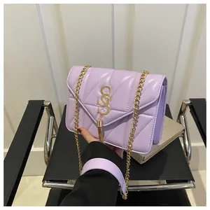Détail du sac à chaîne en cuir matelassé lavande avec pompon doré et logo sur mur blanc
