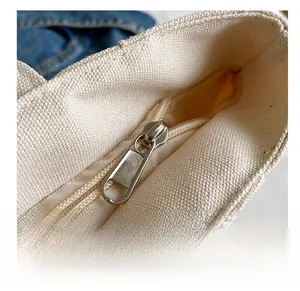 Close-up detail of smooth zipper closure on off-white canvas tote bag showing fabric texture