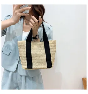 Detail of hand-woven straw tote bag with black canvas handles and V-pattern texture