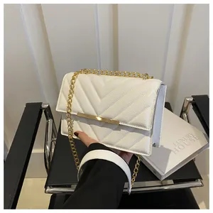 Dettaglio borsa a tracolla bianca trapuntata con catena dorata e barra in metallo su sedia