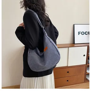 Detail of blue-grey corduroy hobo bag with orange Sport tag showing texture and capacity
