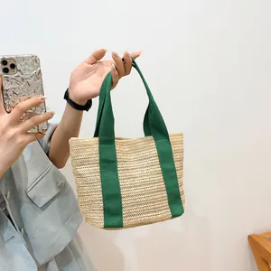 Minimalist straw tote bag with green canvas handles and natural woven texture