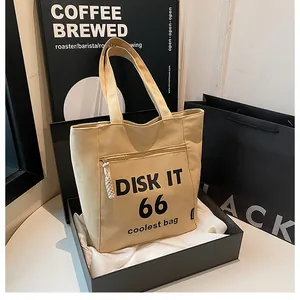 Detail view of beige canvas tote bag with black letter print in a premium gift box