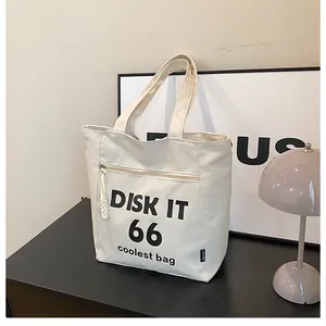 Close-up of cream canvas tote bag featuring front zipper pocket and DISK IT text print