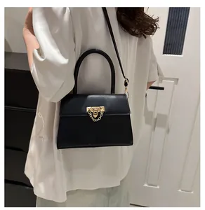 Detail of a chic black leather crossbody bag with elegant gold chain lock on a model