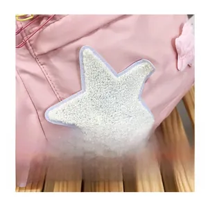 Detail of pink nylon backpack featuring decorative plush star patches and pink straps