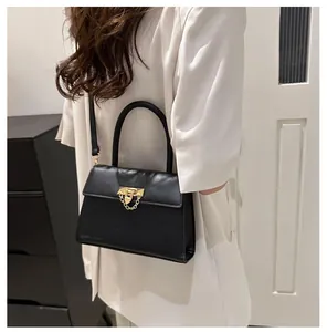 Close-up of black leather handbag with gold metal clasp and chain detail on white blazer