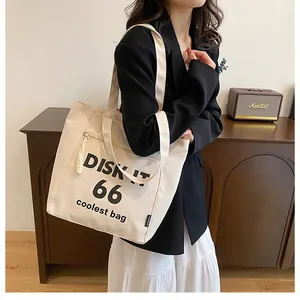 Detailed close-up of cream canvas tote bag featuring black lettering and a zipper front pocket