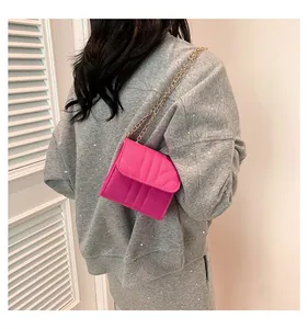 Detail of rose pink quilted chain bag with gold metal strap on a casual grey outfit