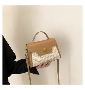 Detail einer handgehaltenen Stroh- und Leder-Patchworktasche mit runder Zierschnalle