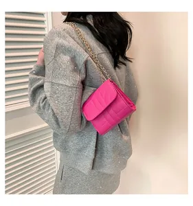Detail of vibrant pink quilted shoulder bag with gold chain strap on grey sweater