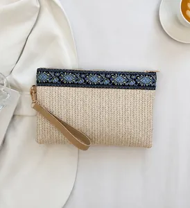 Détail d'une pochette bohème en paille avec broderie bleue et dragonne en cuir
