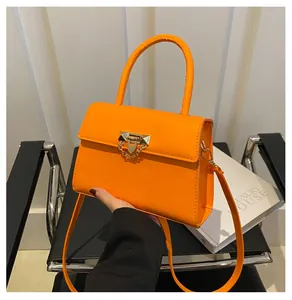 Detail of orange handbag featuring a gold V-shaped metal lock and pyramid stud accents