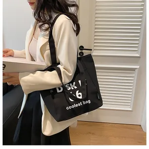 Detail of a large black canvas tote bag with white lettering and comfortable shoulder strap