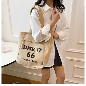 Detail of beige canvas tote bag featuring black lettering and a side zipper pocket
