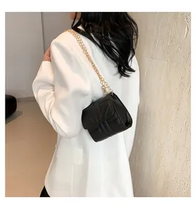 Close-up of black quilted crossbody bag with gold chain strap on white blazer