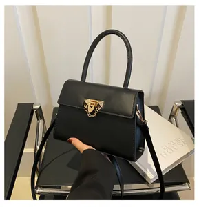 Close-up of black leather square handbag with golden metal lock and chain detail