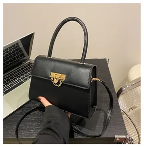 Close-up of black square handbag with golden metal lock and decorative chain on desk