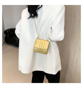 Close-up of golden mini chain bag with geometric stitching on a white blazer outfit