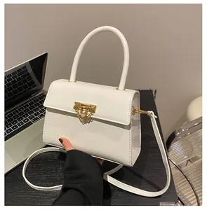 Detail of white crossbody bag with gold trapezoid lock and chain handle in office setting