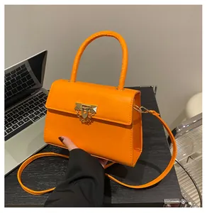 Detail of bright orange crossbody bag with gold lock buckle and metallic chain handle