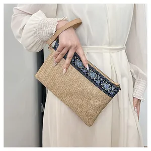 Détail d'une pochette en paille avec tissu à motif ethnique et dragonne en cuir