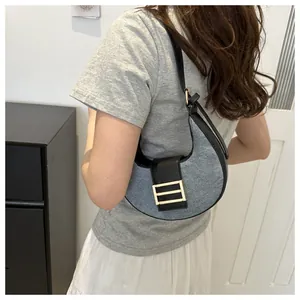 Detalle del bolso de media luna en denim gris con ribete de cuero negro y hebilla dorada