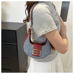 Detalle de correa de cuero rojo y bolso medialuna de mezclilla gris en modelo para look