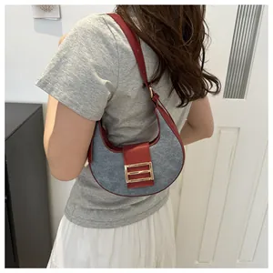 Detalle del bolso de media luna en tela gris con bordes de cuero rojo y hebilla dorada