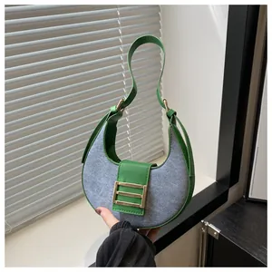 Detalle de bolso medialuna en mezclilla azul con ribetes de cuero verde y hebilla dorada