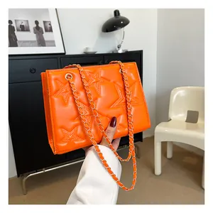 Détail du sac bandoulière orange vif avec motifs d'étoiles surpiquées et chaîne dorée