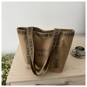 Détail du sac cabas en toile kaki avec imprimé lettres noires sur une surface en bois