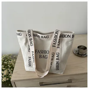Détail d'un sac fourre-tout en toile blanc cassé avec lettrage FASHION BAG noir et fleurs