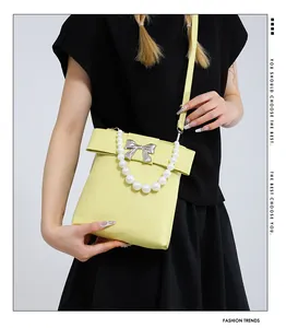 Détail du sac bandoulière jaune avec anse en perles et nœud sur tenue noire