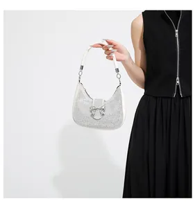 Detail of silver rhinestone crescent bag with metallic bow held by a model in black