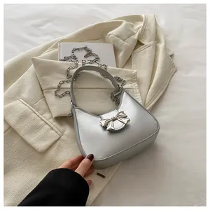 Détail d'un sac à main argenté avec nœud métallique et chaîne sur fond de tissu beige