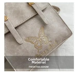Detail showing elegant butterfly embroidery and logo on vintage beige faux leather bag