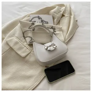 Détail du sac lune blanc avec nœud en métal et bandoulière chaîne sur un blazer chic