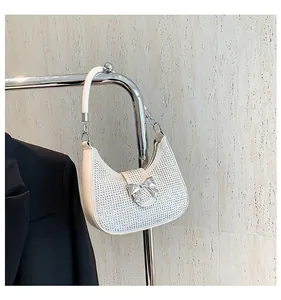 Close-up of a sparkling silver rhinestone bow on a white crescent-shaped shoulder bag