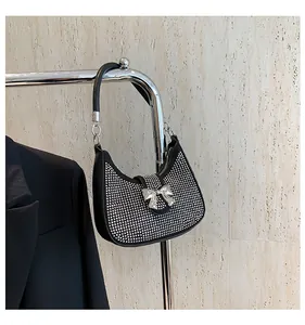 Detail of a black hobo bag featuring silver studs and a metallic bow on stone wall