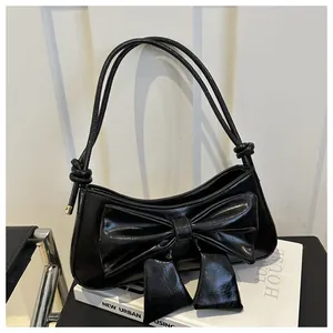 Primer plano detallado del bolso de hombro negro brillante con un gran lazo decorativo