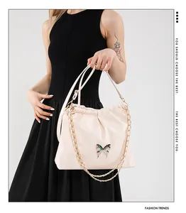 Detail of off-white ruched bucket bag with silver butterfly charm and gold chain strap