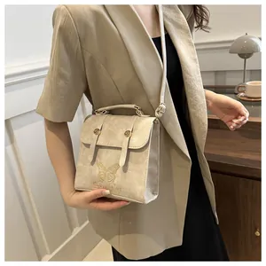 Detail of beige faux leather handbag featuring gold butterfly embroidery and top handle