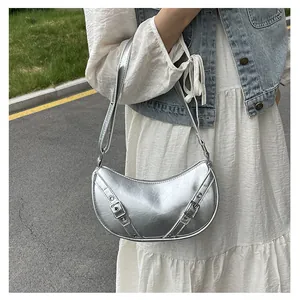 Detail of silver crescent saddle bag with metallic straps and buckle in a street style view