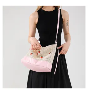 Close-up of handmade straw bucket bag featuring strawberry embroidery and pink leather trim