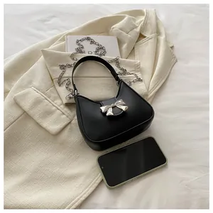 Détails du sac demi-lune noir avec boucle nœud argenté et chaîne, à côté d'un téléphone