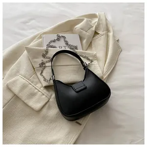 Détail du sac demi-lune noir avec bandoulière chaîne sur un blazer beige chic