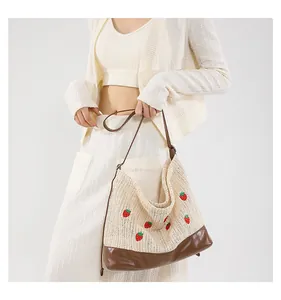 Detail of straw tote bag featuring red strawberry embroidery and brown leather straps