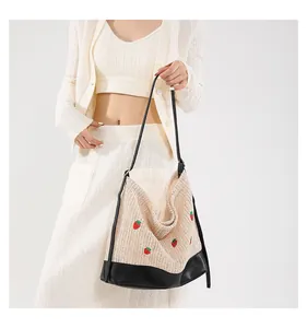 Detail of hand-woven bucket bag featuring red strawberry embroidery and black leather base